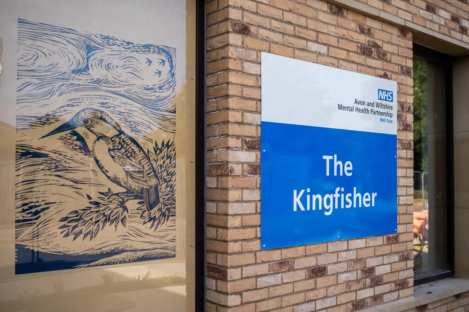 A close-up shot of a window with a kingfisher etching and a blue sign that reads 'The Kingfisher' next to it.